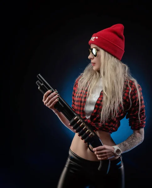 Une blonde lumineuse dans un chapeau rouge avec un fusil de chasse sur un fond sombre — Photo