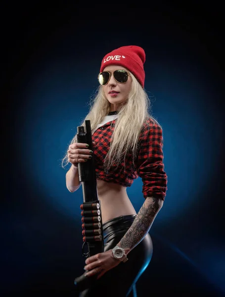 Une blonde lumineuse dans un chapeau rouge avec un fusil de chasse sur un fond sombre — Photo