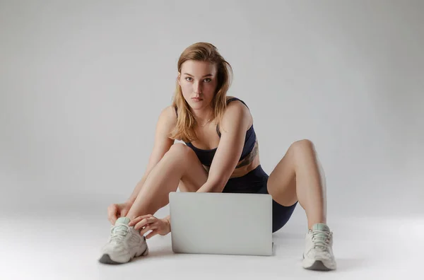 Athletisches Mädchen posiert im Studio und macht online auf einem Laptop vor weißem Hintergrund Übungen — Stockfoto