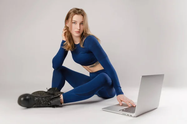 Athletisches Mädchen posiert im Studio und macht online auf einem Laptop vor weißem Hintergrund Übungen — Stockfoto