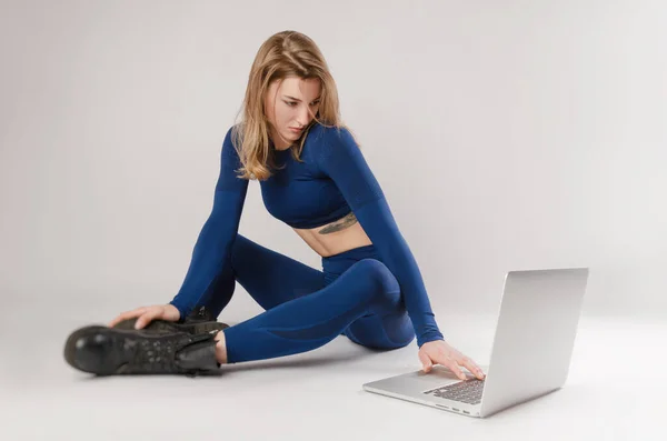 Athletisches Mädchen posiert im Studio und macht online auf einem Laptop vor weißem Hintergrund Übungen — Stockfoto