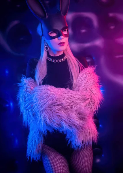 Sexy girl in a bodysuit and fur coat with a rabbit mask in the neon light — Stock Photo, Image
