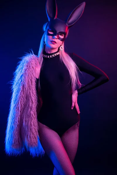 Sexy chica en un body y abrigo de piel con una máscara de conejo en la luz de neón — Foto de Stock