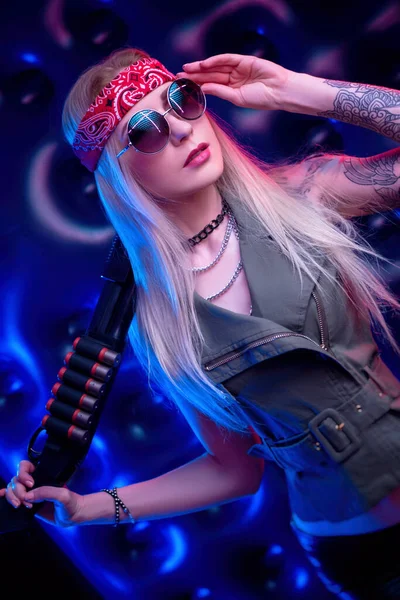 En tjej som ser ut som en hippie med ett hagelgevär i neon — Stockfoto