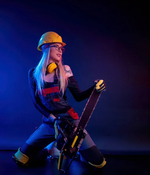 Una chica con una motosierra en un mono sobre un fondo negro en una luz de neón — Foto de Stock