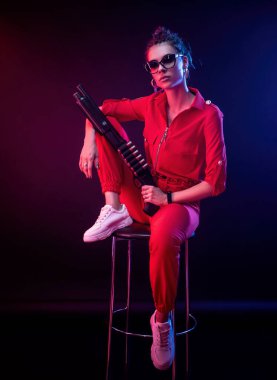 Parlak esmer, kırmızı tulumlu, siyah arka planda bir av tüfeği var.