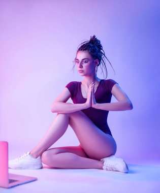 Kafasında rasta desenli bir elbise giyen kız beyaz bir arka planda yerde oturuyor.