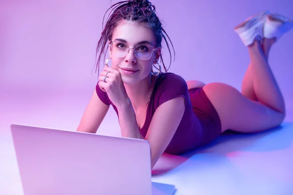 Smukła Dziewczyna Białym Tle Neonowym Kolorze Leży Podłodze Patrzy Laptopa — Zdjęcie stockowe