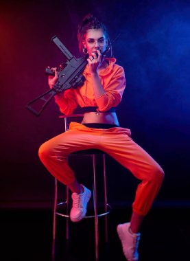 Parlak esmer, turuncu tulumlu ve arka planda makineli tüfekli, neon ışıklı. Radyoda konuşuyor.