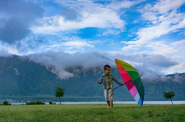 Boy with rainbow umbrella in natural landscape — Stock Photo, Image