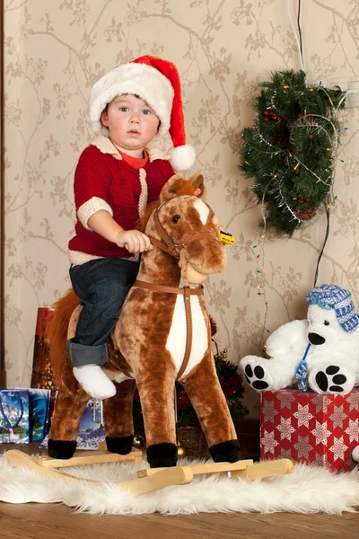 O rapaz senta-se em um brinquedo de um cavalo no quarto — Fotografia de Stock