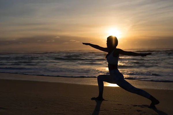 健康的な生活と精神的な開発と体の自然なバランスの概念をビーチでのヨガの練習を行うスポーティな若い女性のシルエット ロイヤリティフリーのストック写真