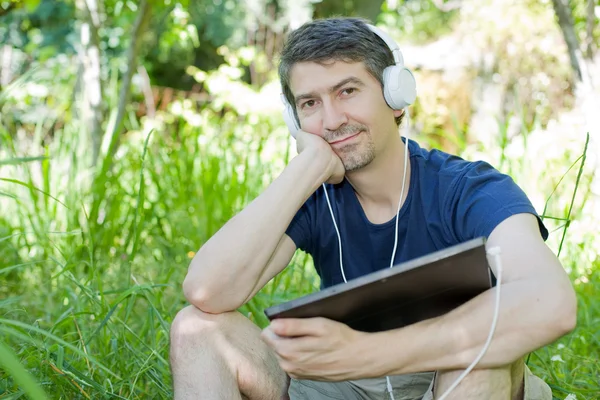 Giovane che si rilassa con un tablet pc ascoltando musica con le cuffie — Foto Stock