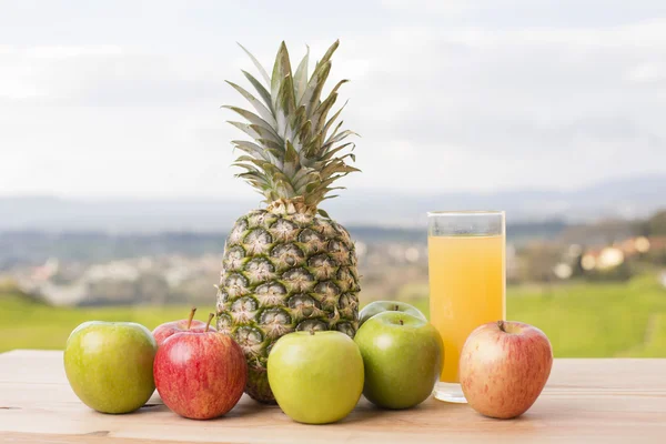 Glas apelsinjuice och massor av frukt på träbord utomhus — Stockfoto