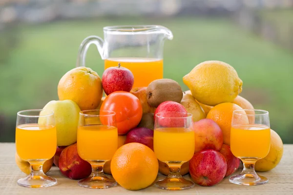 Vasos de jugo de naranja y muchas frutas en la mesa de madera al aire libre —  Fotos de Stock