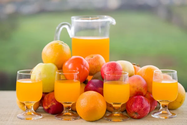 Glazen sinaasappelsap en een heleboel fruit op houten tafel buiten — Stockfoto