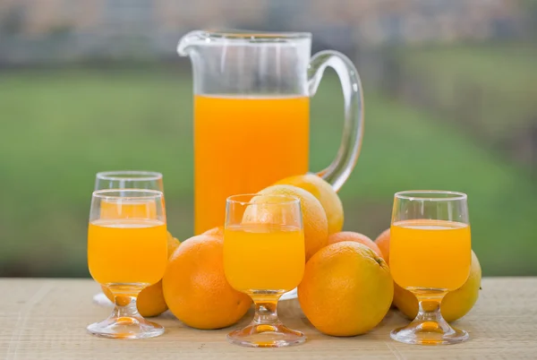 Glas leckerer Orangensaft und Orangen auf dem Tisch im Garten — Stockfoto