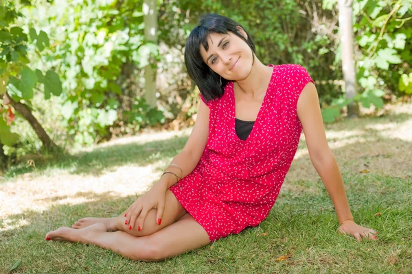 young casual woman posing seated, smiling at the camera, outdoors