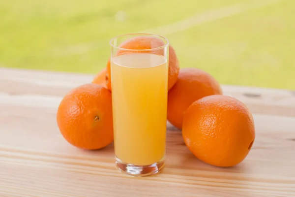 Стакан апельсинового сока и апельсинов на столе в саду — стоковое фото