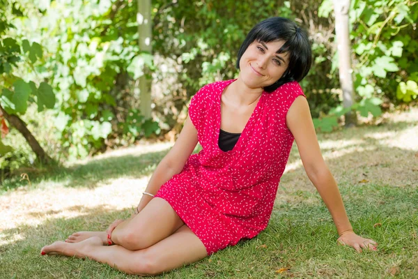 Junge lässige Frau posiert im Sitzen, lächelt in die Kamera, im Freien — Stockfoto