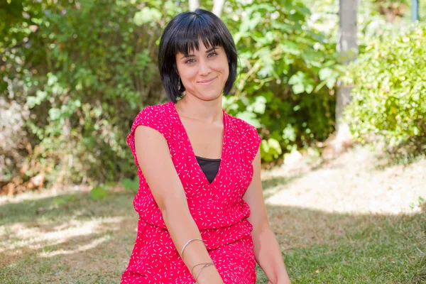 Lässige Frau posiert im Sitzen, lächelt in die Kamera, im Freien — Stockfoto