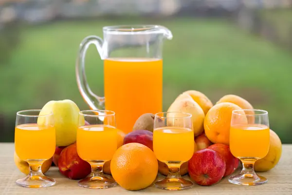 Szklanki soku pomarańczowego i mnóstwo owoców na drewnianym stole odkryty — Zdjęcie stockowe