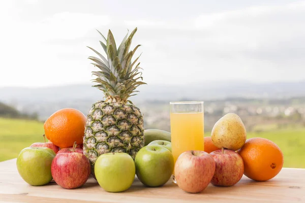 Glas apelsinjuice och massor av frukt på träbord utomhus — Stockfoto