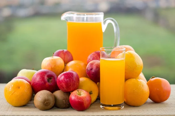 Glazen sinaasappelsap en een heleboel fruit op houten tafel buiten — Stockfoto