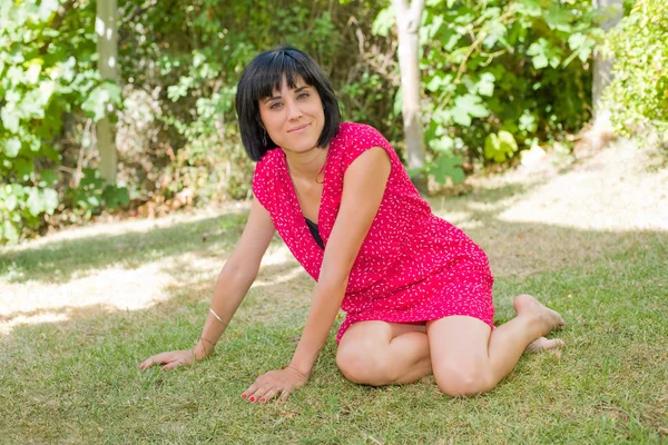 Lässige Frau posiert im Sitzen, lächelt in die Kamera, im Freien — Stockfoto