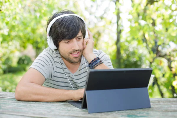 Giovane che lavora con un tablet pc ascoltando musica con le cuffie — Foto Stock