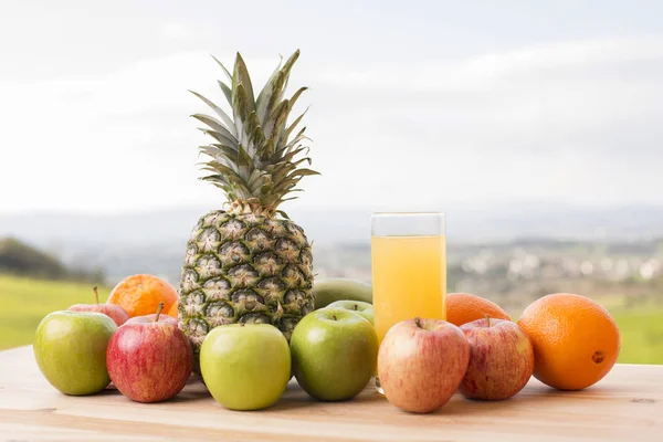 Glas apelsinjuice och massor av frukt på träbord utomhus — Stockfoto
