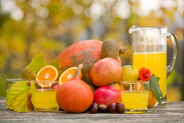 Saftgläser und jede Menge Herbstfrüchte auf Holztisch, draußen — Stockfoto