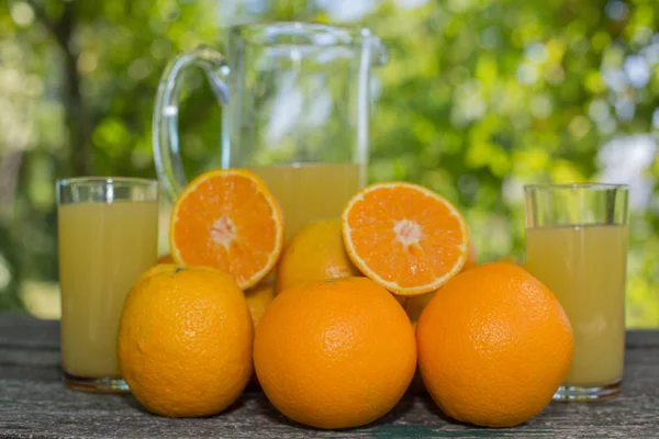 Delicioso jugo de naranja y naranjas en la mesa en el jardín —  Fotos de Stock