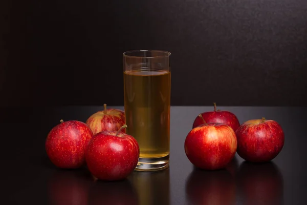 Szklanka soku jabłkowego i czerwone jabłka na ciemnym drewnianym tle — Zdjęcie stockowe