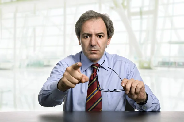 Mad mature business man on a desk, pointing, at the office — Stock Photo, Image