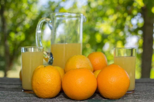Delicioso suco de laranja e laranjas na mesa no jardim — Fotografia de Stock