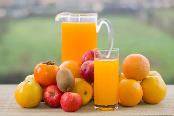 Glazen sinaasappelsap en een heleboel fruit op houten tafel buiten — Stockfoto