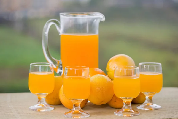 庭のテーブルの上においしいオレンジジュースとオレンジのガラス — ストック写真