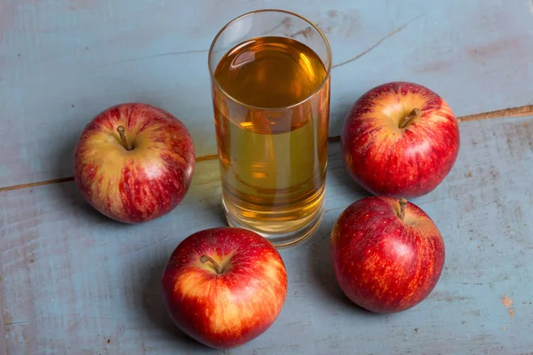 Glas Apfelsaft und rote Äpfel auf blauem alten Holzgrund — Stockfoto