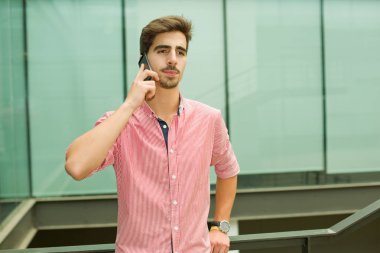 Bir ofis binasının içinde telefonla konuşan sıradan bir genç.