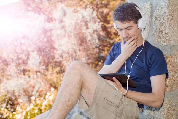 Uomo che lavora con un tablet pc, con cuffie, esterno — Foto Stock