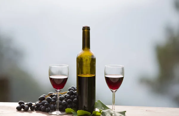 Botella de vino y uvas en mesa de madera al aire libre —  Fotos de Stock