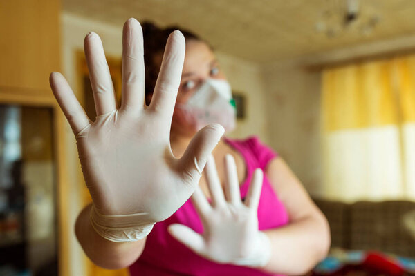 Compliance with the rules of self-isolation of a house. Young girl in a mask and gloves shows stop hands.