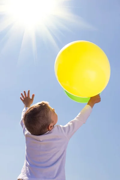 その少年は澄んだ空を背景に風船を手に持ち 手を上に上げて — ストック写真