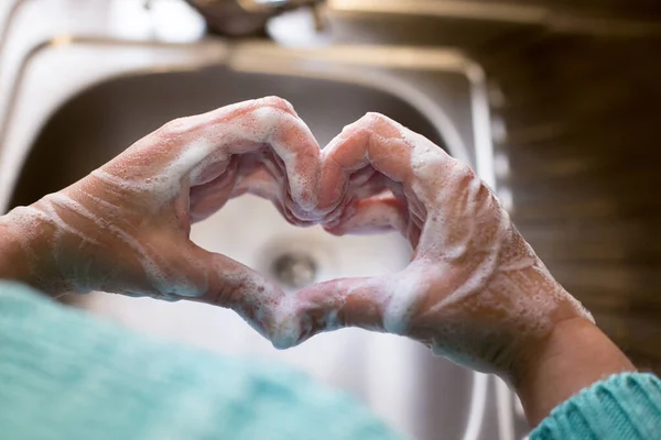 Womans hands made heart shape with soapy hands with sink on background.
