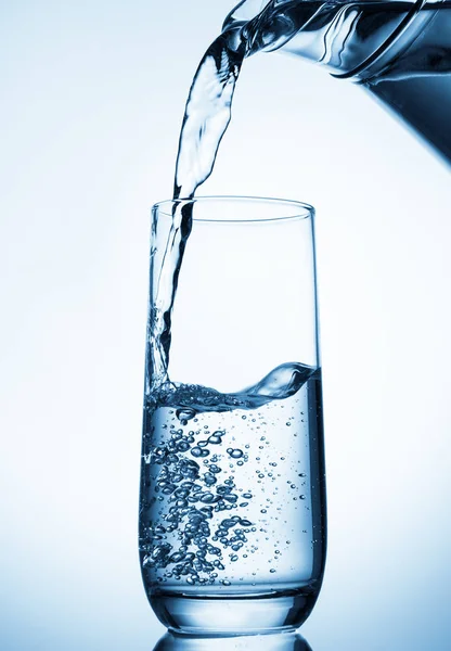 Pouring water from glass pitcher on blue background