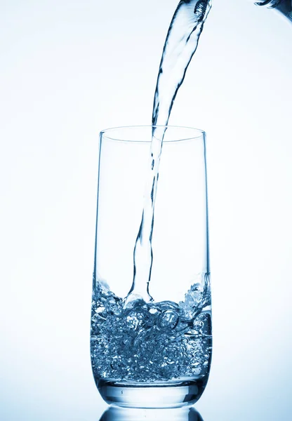 Water pouring into glass on blue background — Stock Photo, Image