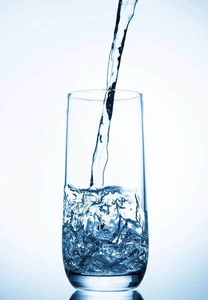 Water pouring into glass on blue background — Stock Photo, Image