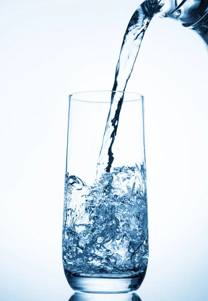 Pouring water from glass pitcher over blue background . — Stock Photo, Image