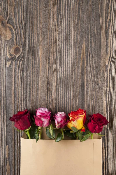 Vícebarevná růže kytice v papírové obálce, přes dřevěné b — Stock fotografie